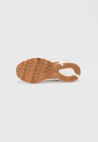 Semelle de chaussure de sport blanche avec une surface en caoutchouc texturé, présentant un motif en nid d'abeille et des accents marron clair. Logo de la marque visible.