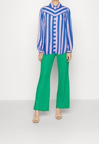 Chemise à rayures rose et bleue avec manches longues, assortie à un pantalon large en velours côtelé vert et des sandales beiges.