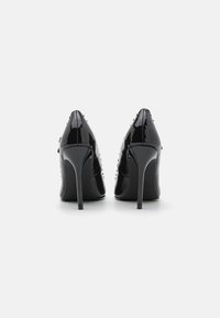 Zwarte lakleren hoge hakken met spitse neuzen, stilettohakken en gespikkelde accenten aan de zijkanten. Gladde textuur en glanzende afwerking.