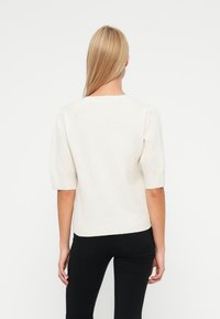 Light cream sweater with short puff sleeves, ribbed hem, and a relaxed fit. Made of soft, textured fabric. Worn with black jeans.