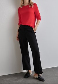 Czerwony sweter z długim rękawem w połączeniu z luźnymi czarnymi spodniami i czarnymi mokasynami z futrzanym obszyciem. Prosty fason o luźnym kroju.