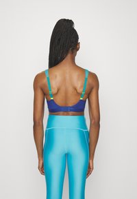 Sostén deportivo azul con tirantes ajustables y un broche en la espalda, combinado con leggings de cintura alta y brillantes en color turquesa con una textura suave.