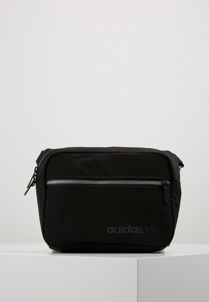 Svart axelremsväska i tyg med en framficka, silvrig dragkedja och präglad adidas-logotyp. Kompakt rektangulär form med minimalistisk design.