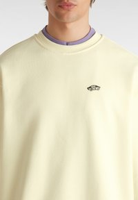 Lichtgele sweatshirt met een ronde hals, voorzien van een zwart Vans logo patch op de borst. De stof lijkt zacht en glad te zijn.