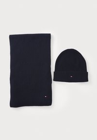 Marineblå ribstrikket tørklæde og hue sæt med et lille logoaccent. Tørklædet er langt og bredt, mens huen har et rullet manschettedesign.