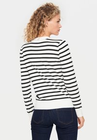 Pull rayé avec des rayures horizontales noires et blanches, col et manches à côtes, associé à un jean en denim foncé. Tissu doux avec une coupe décontractée.
