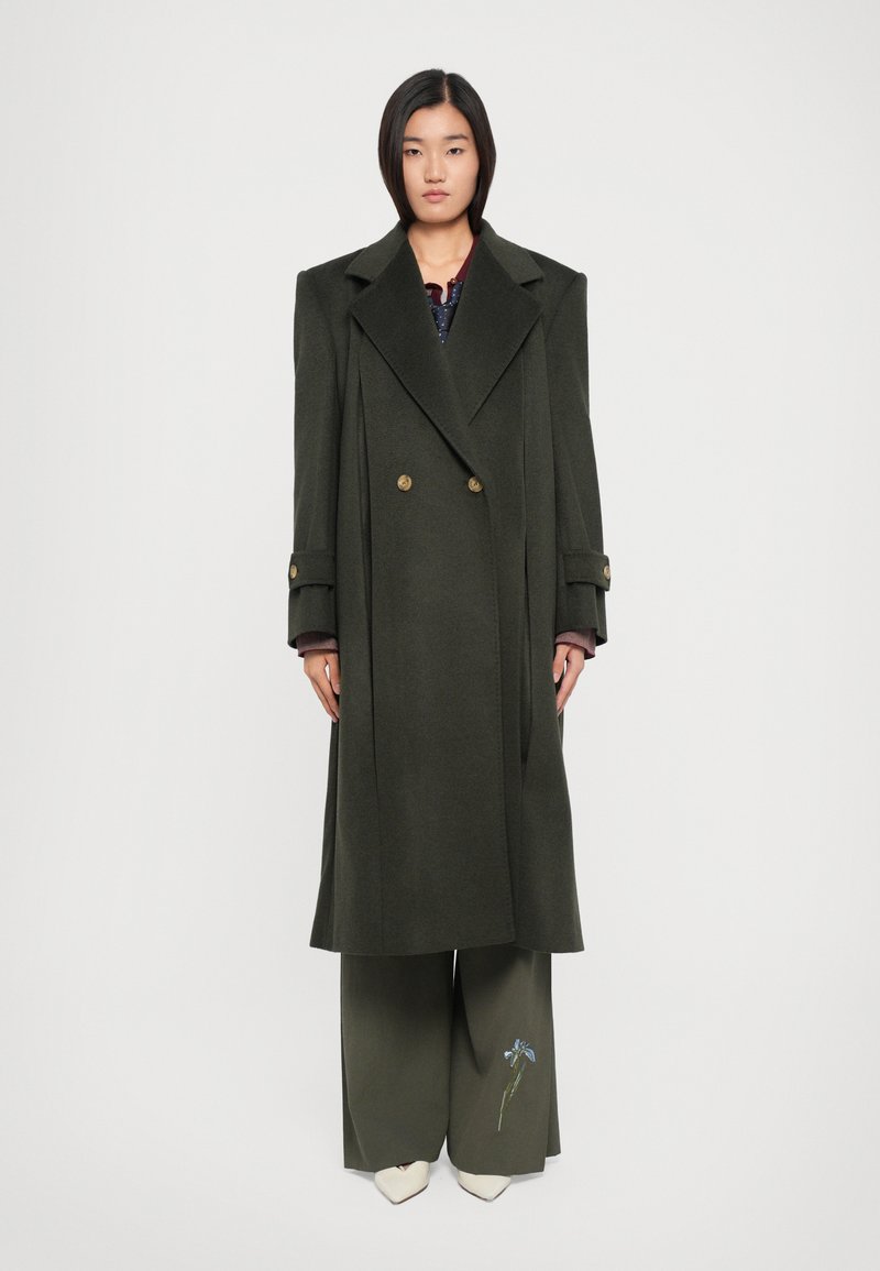 Long manteau en laine vert olive avec une fermeture à double boutonnage, de grands revers et des poignets à boutons, associé à un pantalon à jambes larges ornés de broderies florales.