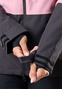 Schwarze und rosa Jacke mit hohem Kragen, Klettverschlussmanschetten und kontrastierenden Streifen. Hergestellt aus glattem, wasserabweisendem Material.