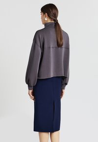 Sweatshirt grigio corto con colletto alto e maniche oversize, abbinato a una gonna aderente blu navy con spacco sul retro.