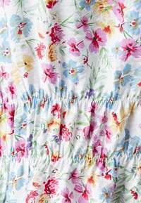 Tessuto stampato floreale con vari colori, tra cui fiori blu, rosa, gialli e rossi su uno sfondo bianco. Dettaglio smock visibile.