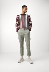 Striped knit sweater with burgundy, beige, and black colors, paired with light green corduroy trousers and beige high-top boots.