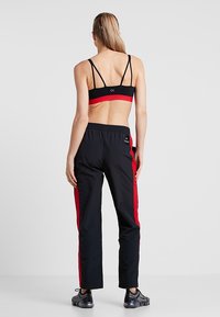 Zwarte sportbeha met rode band; zwarte trainingsbroek met rode zijstrepen; elastische tailleband; glad, lichtgewicht materiaal; minimale merkvoering.
