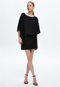 Top negro corto con mangas anchas, combinado con una falda negra ajustada que presenta dos botones decorativos. El material parece suave, de textura mate.