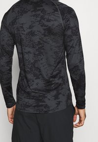 Langarm-Sportshirt in Schwarz mit grauem Tarnmuster, aus einem glatten, dehnbaren Material gefertigt, mit flachen Nähten und einer enganliegenden Passform.