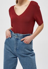 Czerwony, prążkowany top z krótkim rękawem i dekoltem w serek, w zestawieniu z wysokim stanem jasnoniebieskich dżinsów. Subtelna tekstura widoczna na tkaninie.