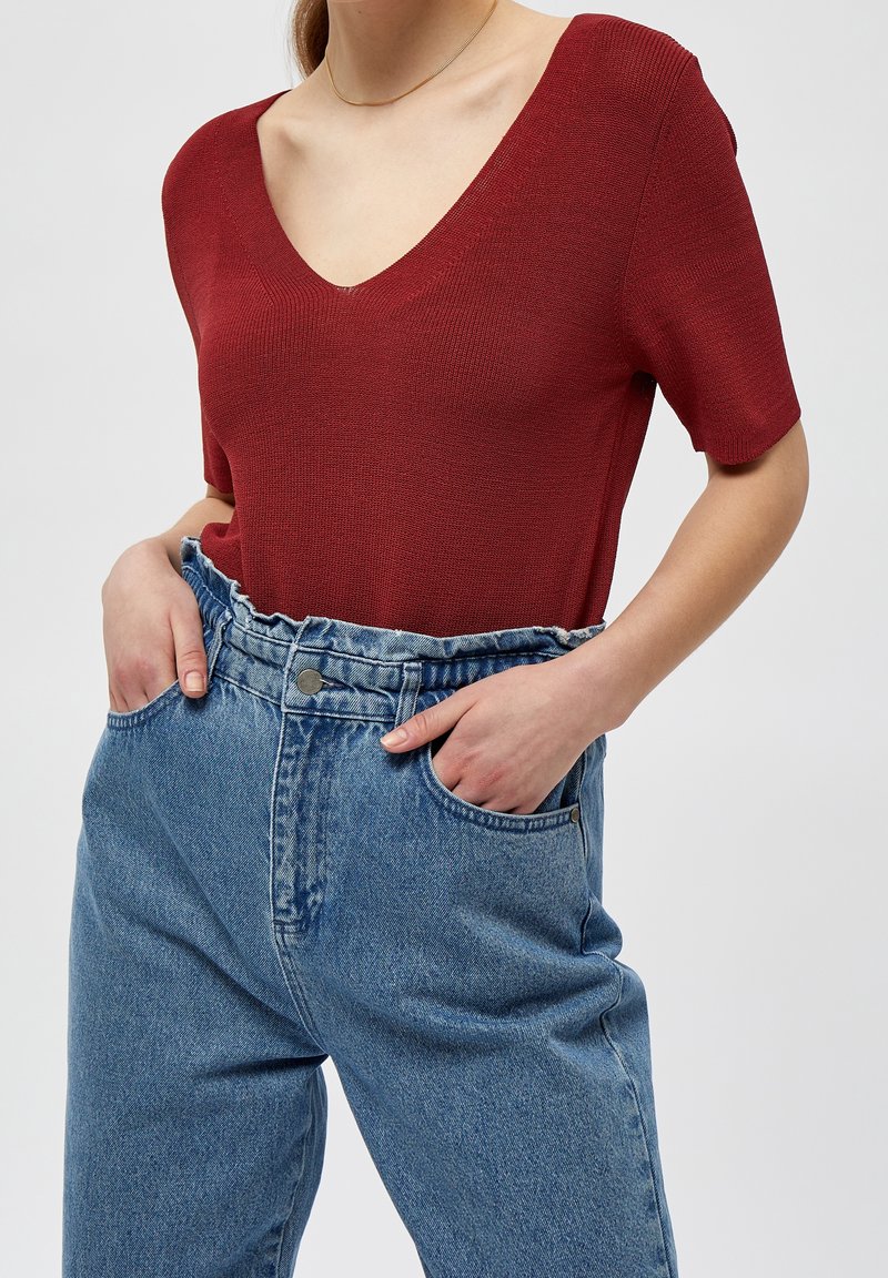 Czerwony, prążkowany top z krótkim rękawem i dekoltem w serek, w zestawieniu z wysokim stanem jasnoniebieskich dżinsów. Subtelna tekstura widoczna na tkaninie.