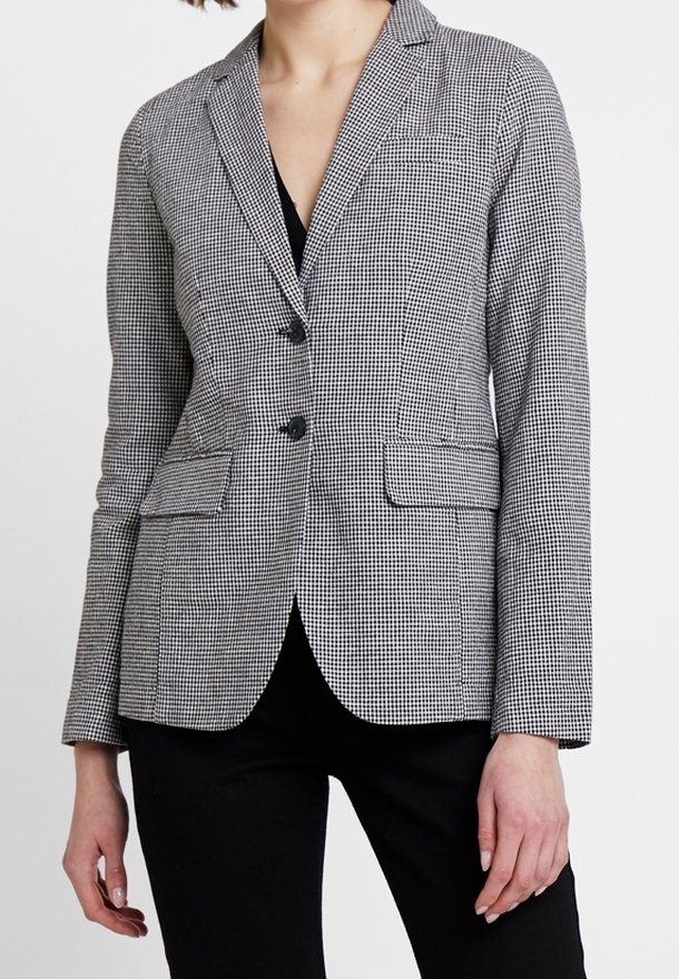 Femme portant un blazer cintré noir et blanc à petits carreaux, avec deux boutons et des poches avant à rabat, par-dessus un pantalon noir.