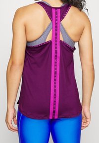 Fialový sportovní tílko s šedými ramínky, s vertikálním pruhem uprostřed a nápisem "UNDER ARMOUR". Hladká textura a uvolněný střih.