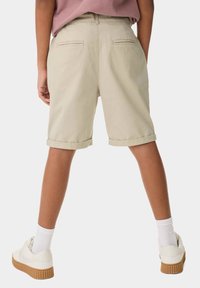 Beige bomullsbyxor med rullad nederkant, två bakfickor och avslappnad passform. Bärs med vita sneakers och ribbade strumpor.