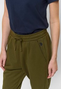 Olijfgroene sweatpants van zacht materiaal, met een elastische tailleband met trekkoord, zijzakken en subtiele geborduurde logodetails.