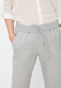 Pantalon en lin gris clair avec une taille élastique, une fermeture à cordon et des poches latérales ; le tissu présente une texture.