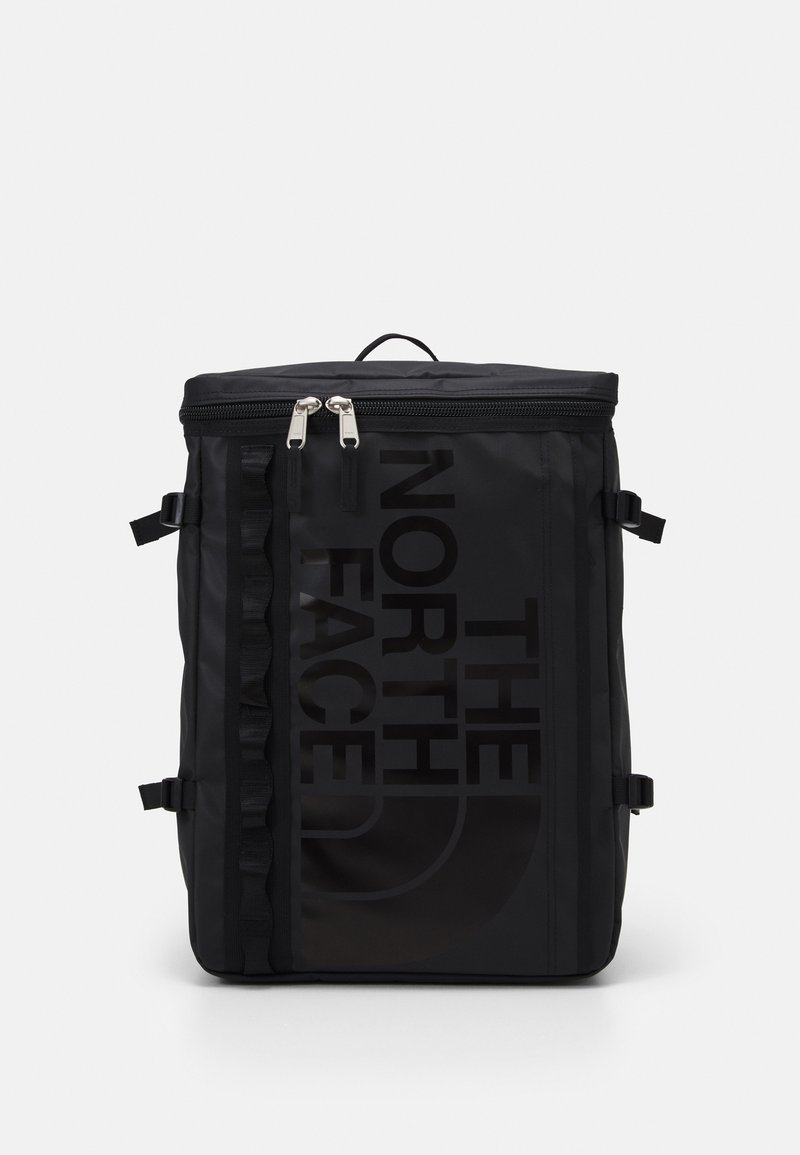 Sac à dos rectangulaire noir avec deux curseurs de fermeture éclair en haut et logo "The North Face" imprimé verticalement sur le panneau avant.