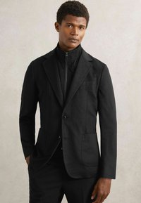 Sort skræddersyet jakke med slim fit, der har en notch revers, to forlommer og et lynlås indre lag. Glat tekstur, ingen synlige mønstre.