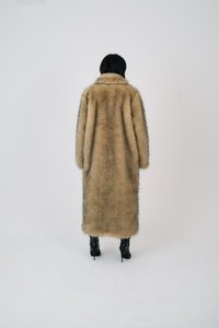 Cappotto lungo in pelliccia sintetica, colore beige con una trama morbida, dotato di un ampio colletto. Abbinato a stivali neri con tacco alto.
