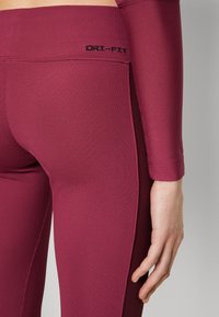 Bordeauxröda ribbade leggings med elastisk midja, som har svart "DRI-FIT"-logotyp och en åtsittande design längs benen.