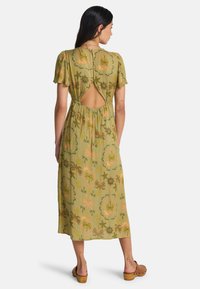 Πράσινο μίντι φόρεμα με κοντά φουσκωτά μανίκια, λεπτομέρεια ανοιχτής πλάτης και λουλουδάτο σχέδιο σε πορτοκαλί και χρυσούς τόνους. Απαλό, ρέον ύφασμα.