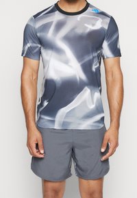 Camisa atlética de manga corta con un patrón abstracto en gris y blanco. Fabricada en un tejido ligero con un cuello negro redondo.