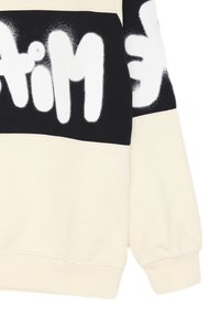 Felpa color crema con un pannello orizzontale nero, caratterizzato da lettere audaci in stile spray bianco sulla parte anteriore e sulla manica.