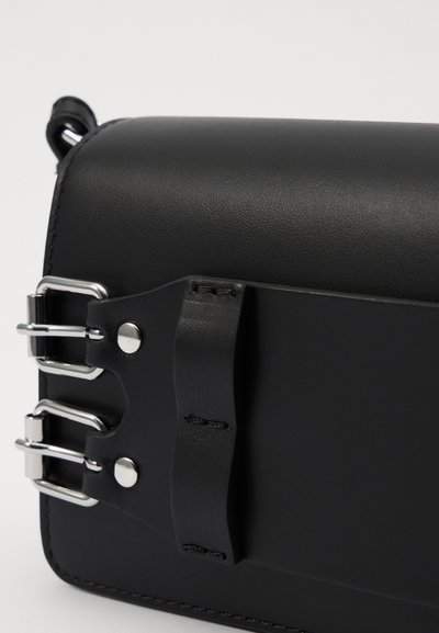 Borsa in pelle nera con una texture liscia, contraddistinta da accessori in metallo argentato, quattro elementi a forma di fibbia e dettagli cuciti lungo il bordo.