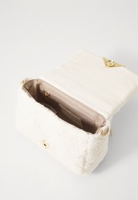 Hvid, fluffy stofpose med quiltet design, guldfarvede hardware og en beige satinforing. Har en indre lomme til opbevaring.