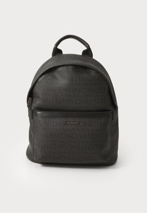 Mochila preta com design de logótipo em relevo. Possui um bolso frontal com fecho, forma arredondada e alças duplas ajustáveis para transporte.