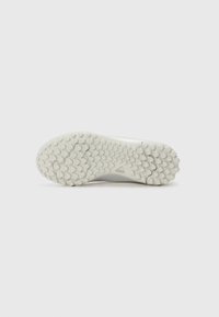 La semelle d'une chaussure de sport blanche présente une surface texturée avec un motif hexagonal et un logo discret. Le design met l'accent sur l'adhérence et la durabilité.