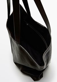 Zwarte leren handtas met twee stevige handvatten, zachte textuur en een open bovenkant die een zwart interieur met een ritsvak onthult.