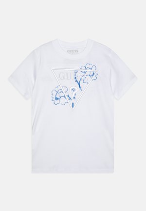 Valge puuvillane T-särk, millel on kolmnurkne sinine tikandiga kujundus koos tekstiga "GUESS," ümbritsetud siniste lillede aktsentidega. Lühikesed varrukad.