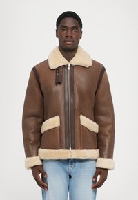 Veste en shearling marron avec col et manchons en fourrure beige. Comprend une fermeture éclair centrale, deux poches avant et des accents marron contrastants.