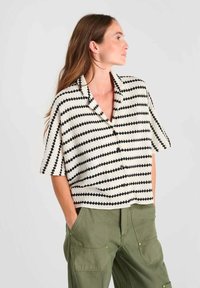 Korte mouwen shirt van gebreid materiaal met een zwart-wit zigzagpatroon, voorzien van een kraag en een sluiting met knopen aan de voorkant.