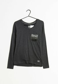 Grå långärmad skjorta med rund halsringning och en ficka prydd med svarta och silverfärgade paljetter. Tyget är mjukt och något texturerat.