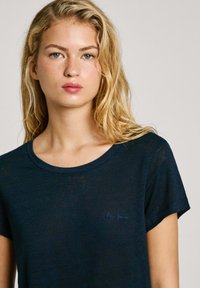 Tumši zila īsām piedurknēm t-krekls ar apaļu kakla izgriezumu un mazu izšūtu "Pepe Jeans" logo zilā krāsā uz krūtīm. Mīksts, teksturēts audums.