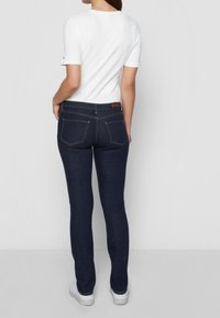 Jeans oscuros ajustados, con bolsillos traseros y costuras decorativas. Combinados con una camiseta blanca lisa y zapatillas blancas.
