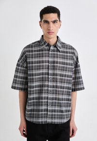 Camicetta a maniche corte con bottoni in un motivo a quadri nero e grigio. Presenta un colletto classico e un design a vestibilità rilassata con una leggera lucentezza.