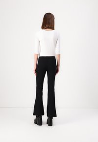 Černé zvonové kalhoty z elastického materiálu, spárované s bílým topem s dlouhým rukávem. Tento outfit má slim fit a délku po kotníky.