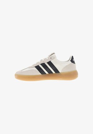 White and beige sneaker with black stripes and gum sole, low-top design, lace-up closure, and branded heel tab.