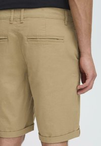 Pantalones cortos de algodón caqui con corte recto, dobladillos enrollados y dos bolsillos traseros. Tejido suave con una textura sutil.