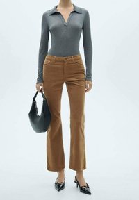 Polo gris à manches longues avec patte de boutonnage ; pantalon évasé en velours côtelé marron ; tenant un sac à main noir incurvé ; portant des escarpins noirs pointus.