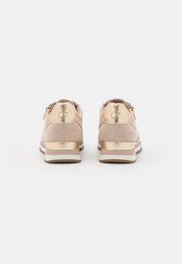 Un paio di sneaker in suede beige con dettagli metallici dorati sul tallone e zip, mostrati da dietro su uno sfondo bianco.