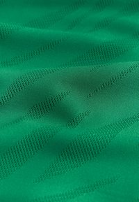 Tissu vert avec un motif texturé de petites perforations verticales et diagonales créant des rayures subtiles et des ombres légères.